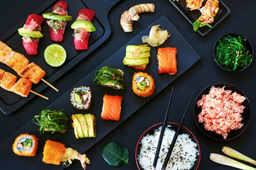 Top view of assorted sushi rolls with salmon, avocado and wakame, beef steak in a pan, grilled salmon, tuna sushi, crab meat, steamed rice in a bowl and wakame salad. 