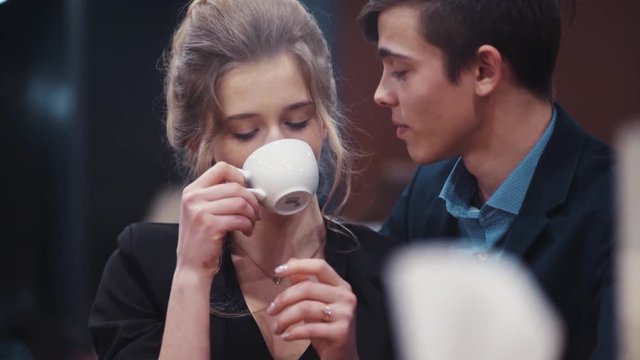 A pretty nice girl drinking coffee on a date and listening to her young boyfriend who is then kissing her.