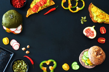 Food frame of assorted healthy sandwiches with guacamole, radish, cucumber, tomato, pepper and seasoning on a dark table. Copy space. 