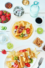 Healthy breakfast with crepes, exotic fruit, coffee and milk over white background. Thin pancakes with starfruit, dragon fruit, strawberry, banana, lime and honey. 
