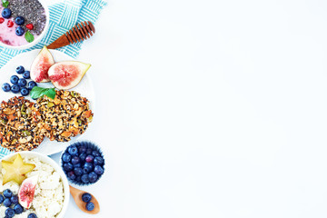 Top view of wholegrain cookies, yoghurt with chia, soft ricotta with blueberry, figs and carambola on a white table. Healthy breakfast with a copy space.