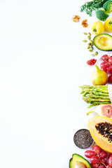 Vertical top view of fresh fruit and veggies, nuts, seeds, superfoods on a white background with a copy space. Clean eating or raw diet concept. 