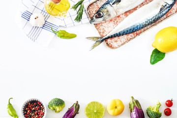 Raw mackerel fish in salt, fresh vegetables, olive oil, herbs and spices on white background with copy space. Ingredients for light dinner or supper. 
