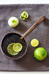 Vertical top view of morning detox water with lime in rustic coconut bowl om dark fabric...