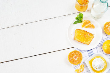 Portion of orange sponge cake with jam, fresh milk and mandarin on white table with copy space.