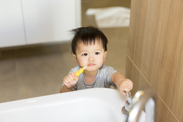 Asian baby uses toothbrush