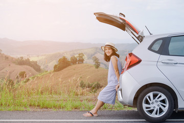 Fototapeta premium Woman traveler sitting on hatchback car with mountain background in vintage tone