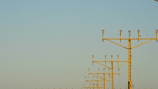 Airplane landing at airport at sunset with row of lamp posts