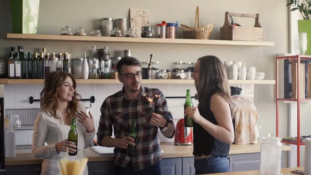 three multi-race friends is having a perty with beer and sparkler in a home kitchen