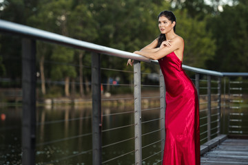 Beautiful young woman in the gardens wearing a long silk red dress.