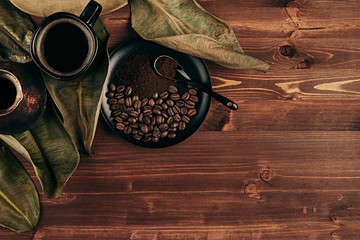 Fototapeta na wymiar Hot coffee in black cup with beans, dry leaves and turkish pot cezve with copy space on brown old wooden board background, top view. Rustic style.