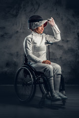 Female fencer in wheelchair holds safety mask and a sword.