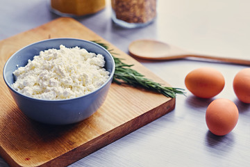 Curd in a cup, eggs and wooden spoon lying on a table.
