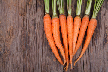 Bunch of fresh carrots with green leaves over wooden background