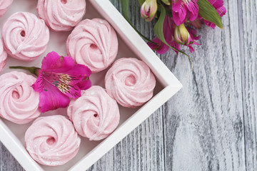 Pink zephyr in gift box and pink flowers on grey wooden background