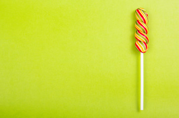 Bright juicy colored lollipop on a green background. Lollipop  in the form of a color spiral. Fruit...