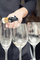 Sommelier pouring white wine to the wine glass. Serving table prepared for event party or wedding. Soft focus, selective focus. Toned.
