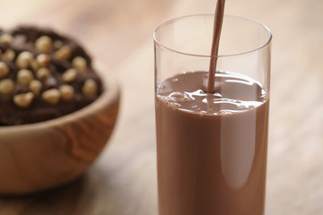 pouring chocolate milk in glass with homemade chocolate cookies with hazelnuts on background, focus...