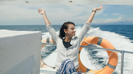 Young beautiful female traveler in casual clothing is having cruise on board of a yacht at the open...