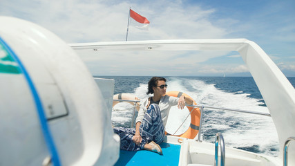 Cute girl sitting in the back of a motor boat enjoys walking on the ocean. Young woman in sunglasses look around and smiles. Tourist on a yacht while sailing.