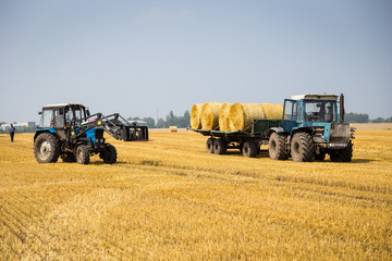 Fototapeta na wymiar Vinnitsa,Ukraine - July 26,2016.huge tractor collecting haystack in the field at nice blue sunny day,Tractor collecting straw bales,Agricultural machine collecting bales of hay,harvest concept