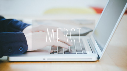 Merci, French text for Thanks text over young man typing on laptop at desk