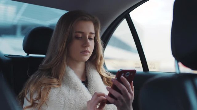 Pretty beautiful blonde with loose hair texting on her phone whilst driving in her modern car from work.