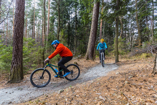 Mountain biking women and man riding on bikes in early spring mountains forest landscape. Couple cycling MTB enduro flow trail track. Outdoor sport activity.