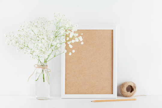 Mockup of picture frame decorated gypsophila flowers in vase on white working table with clean space for text and design your blogging.