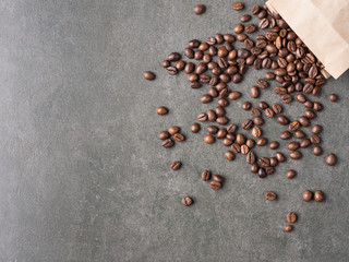 Roasted coffee beans scattered from paper bag over dark gray granite plate, captured from top view with sharp focus