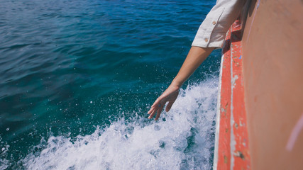 Fototapeta premium Woman waving her hand over the sea waves during motion of the boat. On board the old motorboat peeled off paint.