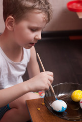 A little boy paints the eggs on the eve of Easter, colorful paints and brush,