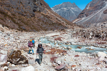 Fototapeta premium Three Hikers walking on rocky Footpath along wild Mountain River