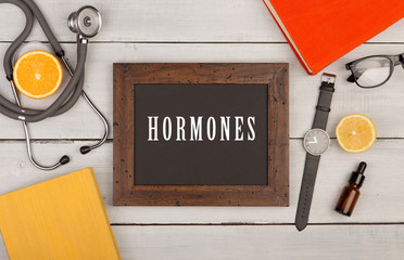 blackboard with text "Hormones", books, stethoscope and watch