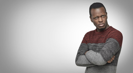 Studio portrait of skeptical African American young male in casual sweater looking with suspicious...