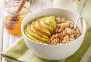 Organic oatmeal into a ceramic bowl with Apple, cinnamon and honey on white wooden table. Healthy Breakfast - the concept of proper nutrition and diet. Selective focus