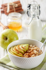 Organic oatmeal into a ceramic bowl with Apple, cinnamon and honey on white wooden table. Healthy Breakfast - the concept of proper nutrition and diet. Selective focus