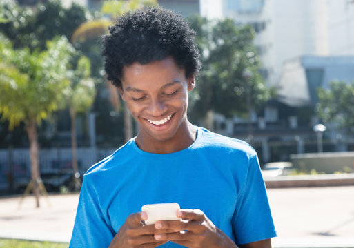 Laughing young african american man sending message with mobile phone
