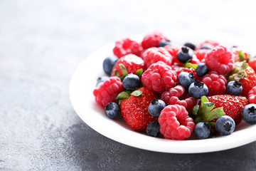 Fresh and sweet berries in white plate on grey background