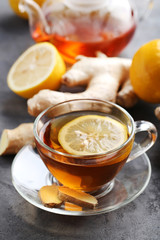 Cup of tea with ginger root and lemon on grey wooden table