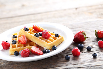 Homemade waffles with berries in plate on grey wooden table