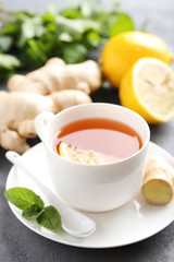 Cup of tea with ginger root and lemon on grey wooden table