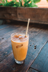 Close up of glass of cold coffee with ice and pinstripe on the wooden textured table