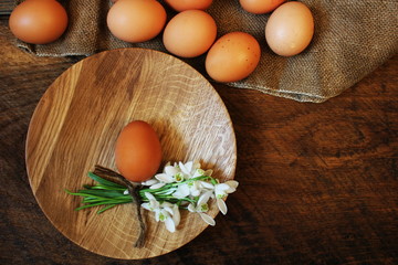 Easter background. Rustic wooden table with plate, egg, flowers and cutting board . Top view.