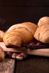 Croissants on board on wooden background. Rustic style. Piece of chocolate.