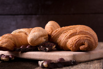 Croissants on board on wooden background. Rustic style. Piece of chocolate.