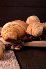 Croissants on board on wooden background. Rustic style. Piece of chocolate.