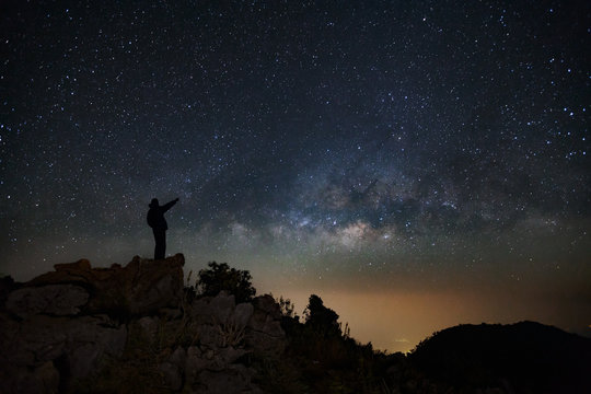 A Man is standing next to the milky way galaxy pointing on a bright star on Doi Luang Chiang Dao mountain, Long exposure photograph, with grain