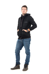 Serious confident male model in black hooded jacket with hands in pockets. Full body length portrait over white studio background.