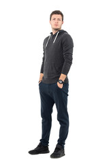 Serious frowning man in sportswear with hands in pockets looking at camera. Full body length portrait over white studio background.